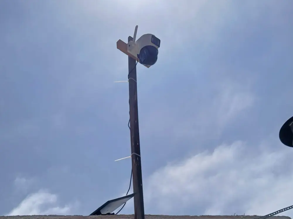 Cámara PTZ blanca montada en lo alto de un poste de madera contra el cielo, alimentada por panel solar